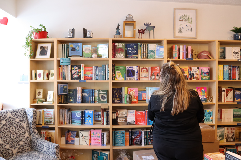 A person standing in front of a book shelf shopping for books.