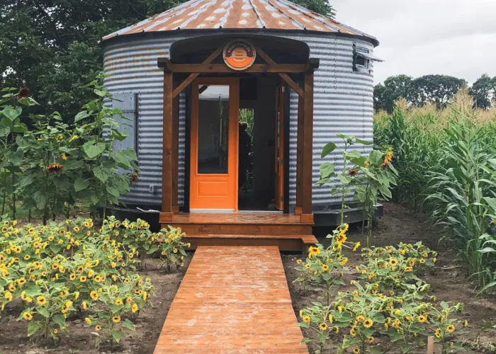 Enright Cattle Company. A tin silo shaped shed with a ramp and orange door. Flowers surrounding it.